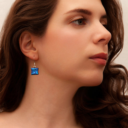 Close-up of woman wearing matching blue florentine dichroic glass drop earrings from Invoke London’s Astra collection.
