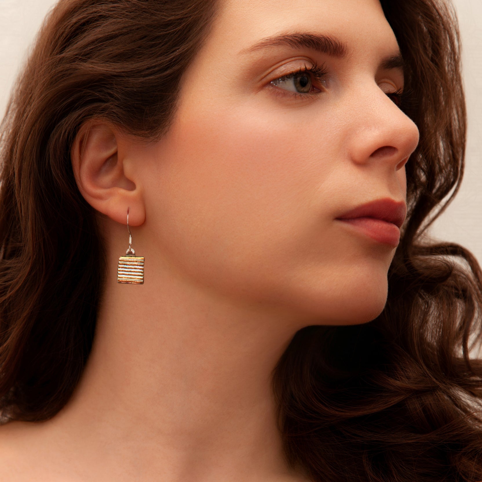 Model wearing gold striped dichroic glass drop earrings from the Astra Collection, radiating warm golden hues.