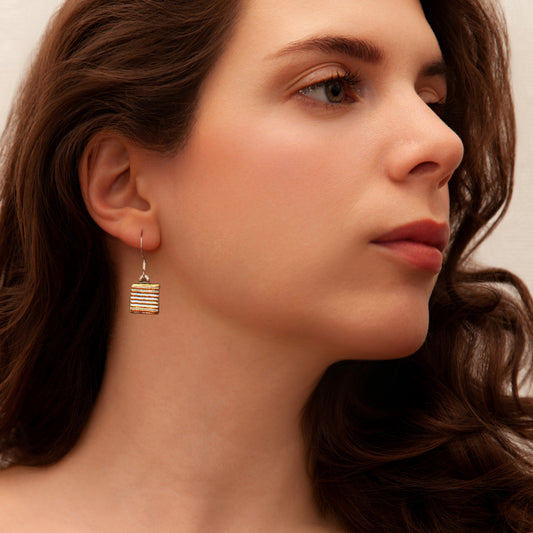Model wearing gold striped dichroic glass drop earrings from the Astra Collection, radiating warm golden hues.