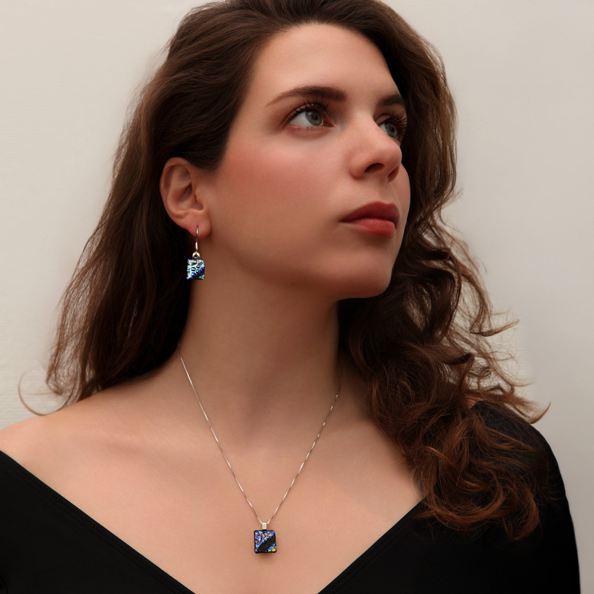 Model wearing matching dichroic glass necklace and drop earrings in shimmering peacock tones – handmade by Invoke London.