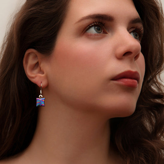 Close-up of woman wearing pink and blue dichroic glass drop earrings with bubble texture from the Astra collection by Invoke London.