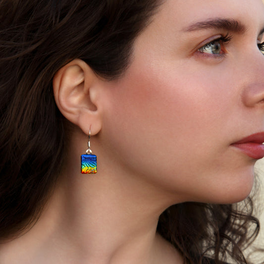 Woman wearing square rainbow florentine dichroic glass drop earrings from the Astra collection by Invoke London – handmade in London.