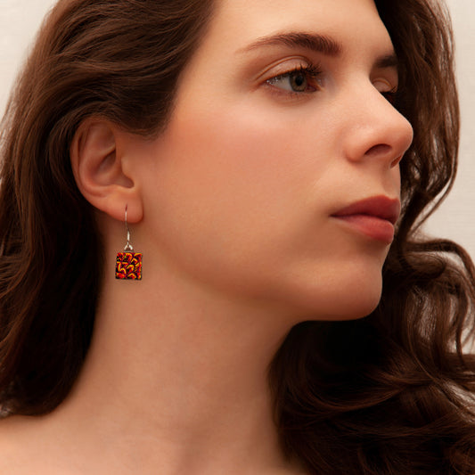 Close-up of model wearing red-orange dichroic glass drop earrings with shimmering detail from the Astra Collection by Invoke London.