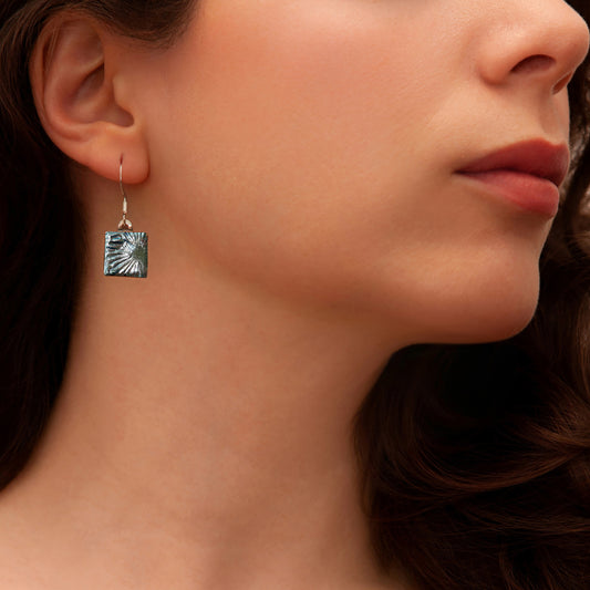 Close-up of a woman wearing a handcrafted silver florentine dichroic glass drop earring from the Astra collection by Invoke London.