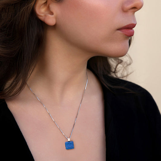 Woman wearing a necklace with a blue pendant against a neutral background