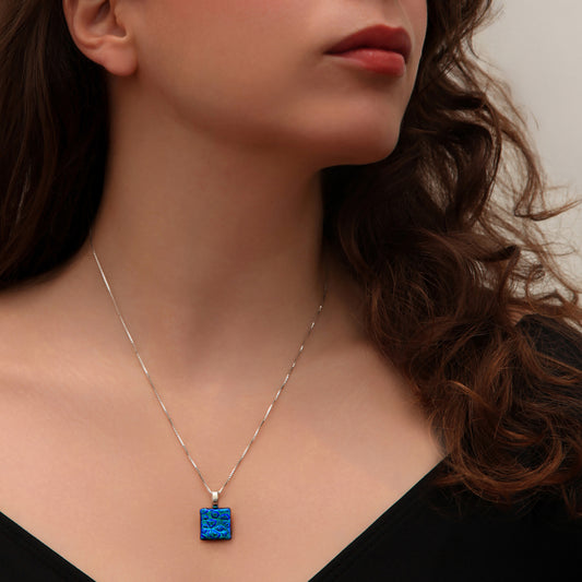 Close-up of woman wearing square blue dew drop dichroic glass pendant necklace from the Astra collection by Invoke London – handmade in London.