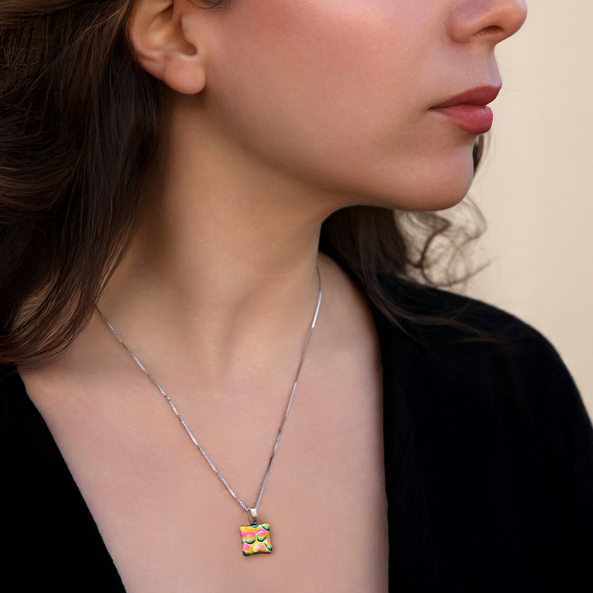 Close-up of woman wearing gold and pink bubbles dichroic glass square pendant necklace from the Astra collection by Invoke London.