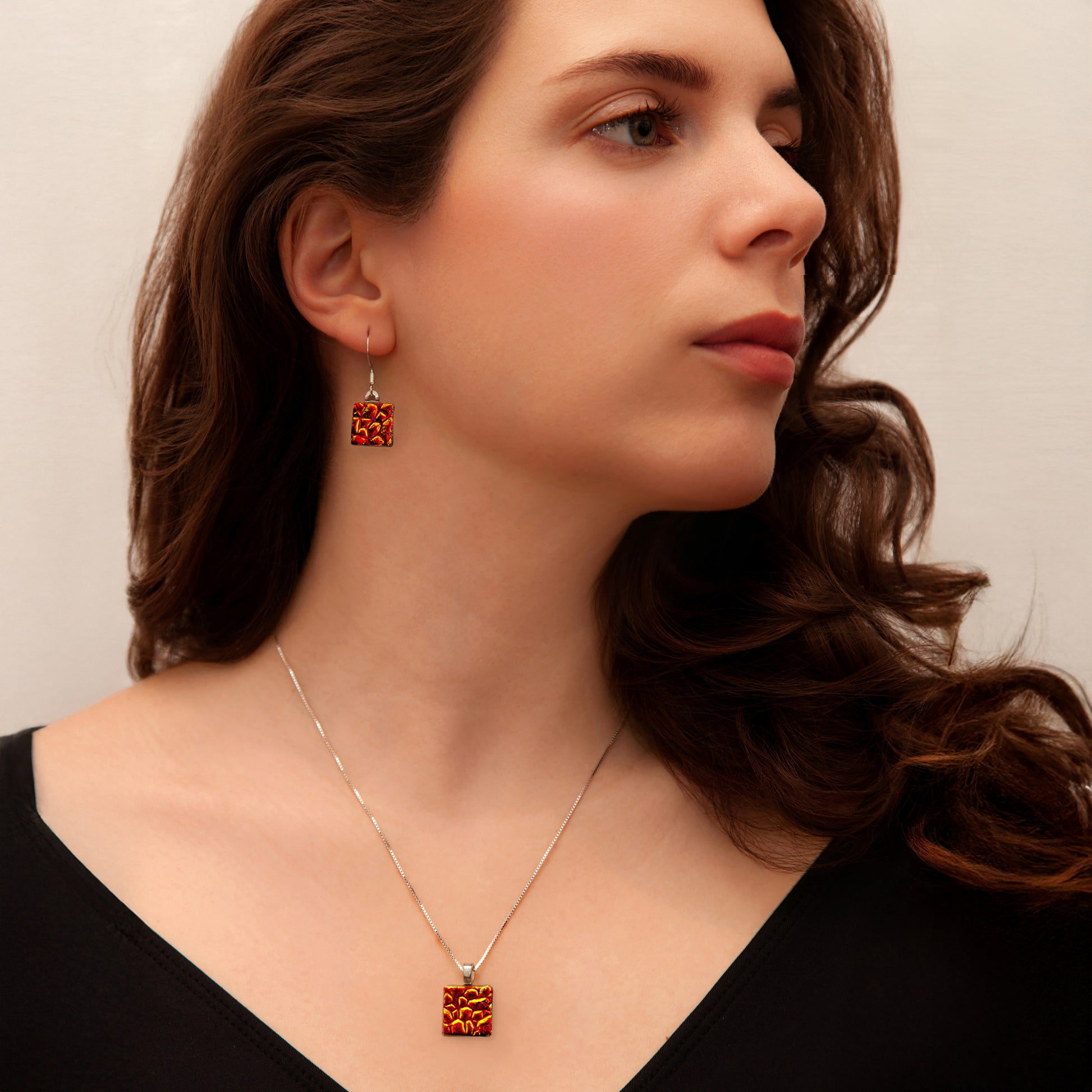 Model showcasing a matching necklace and drop earrings set in vibrant red-orange dichroic glass from Invoke London’s Astra Collection.