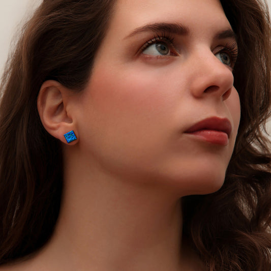 Close-up of woman wearing square blue dew drop dichroic glass stud earrings from the Astra collection by Invoke London – handmade in London.