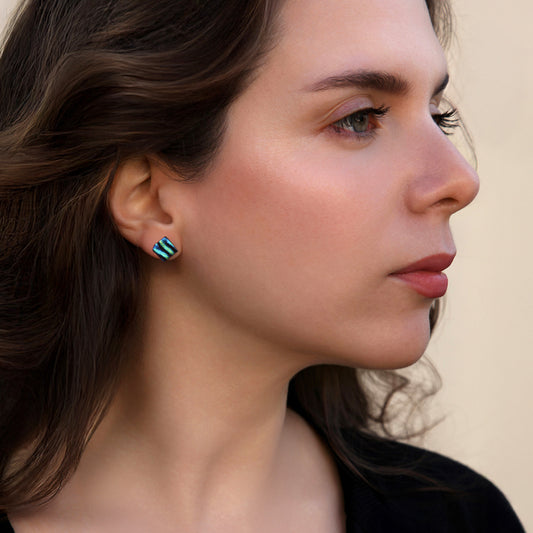 Close-up of a woman wearing blue and green ripple dichroic glass stud earrings from the Astra collection by Invoke London.