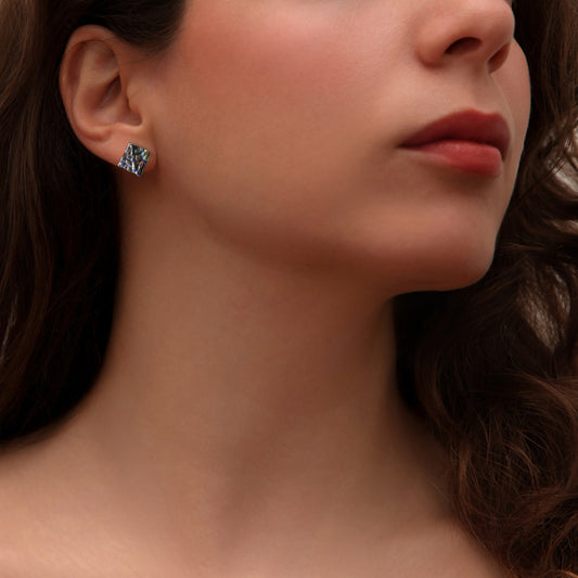 Close-up of handmade dichroic glass stud earring in peacock blue and violet hues – sustainable jewellery by Invoke London.