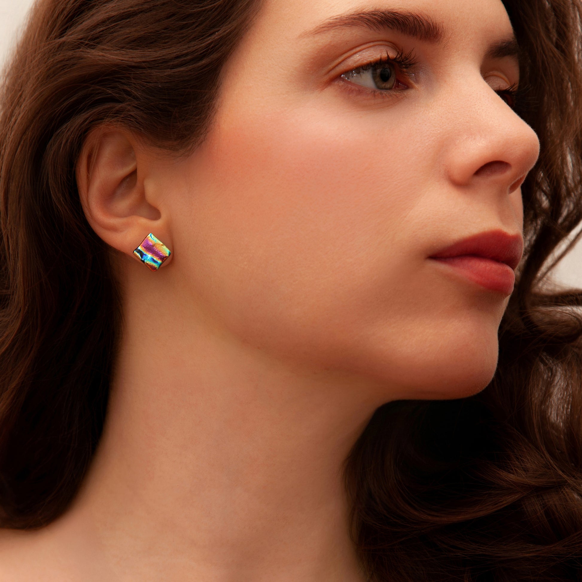 Close-up of model wearing pink ripple dichroic glass square stud earrings, catching the light with a vibrant, shimmering finish.