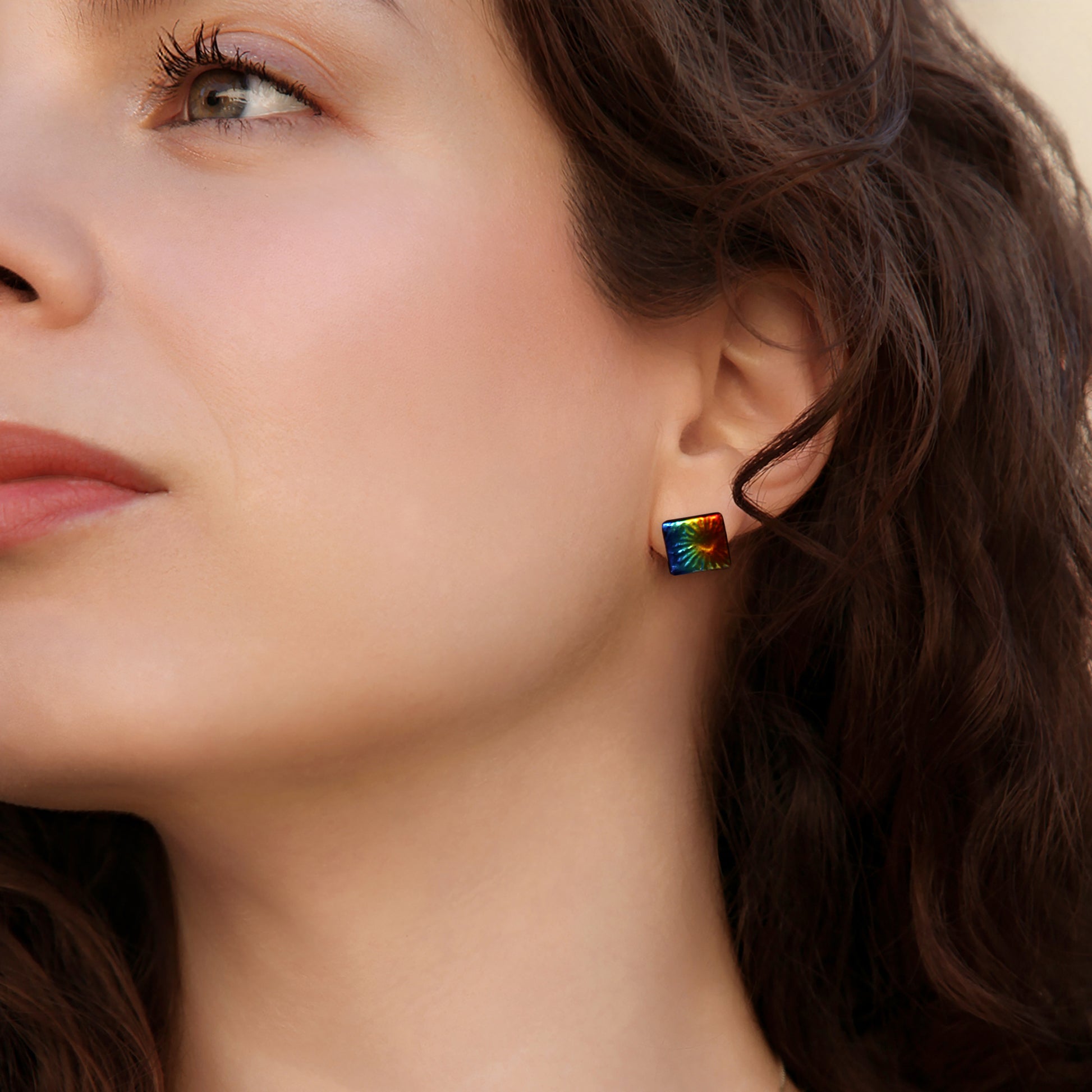 Close-up of woman wearing square rainbow florentine dichroic glass stud earrings from the Astra collection by Invoke London.