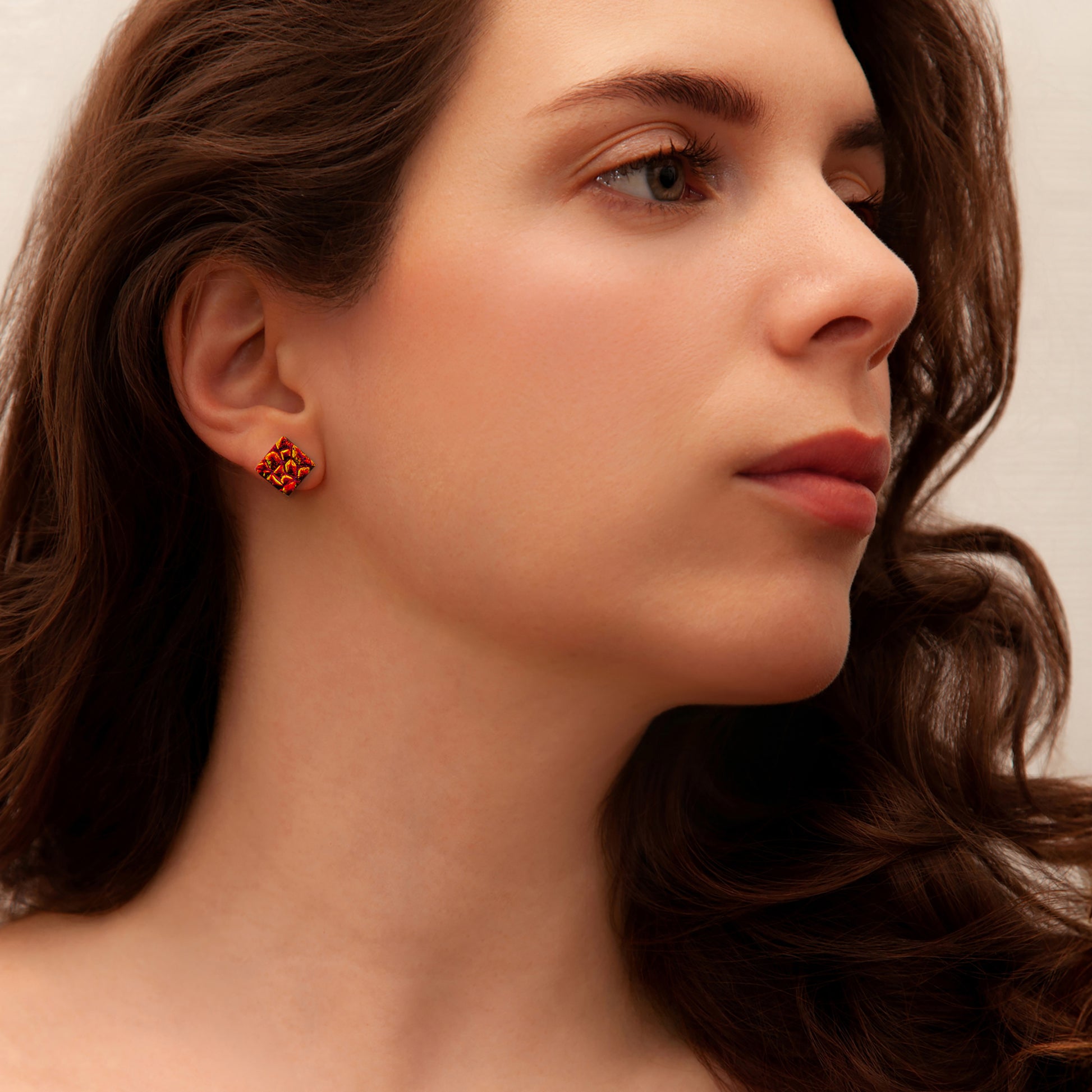 Model wearing a red-orange dichroic glass stud earring from the Astra Collection, handmade by Invoke London.