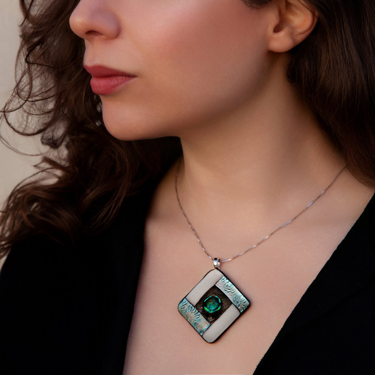 Close-up of a woman wearing the Elementa Air necklace by Invoke London, featuring a handcrafted diamond-shaped fused dichroic glass pendant in shimmering whites and silvers to symbolise clarity, lightness, and peace.