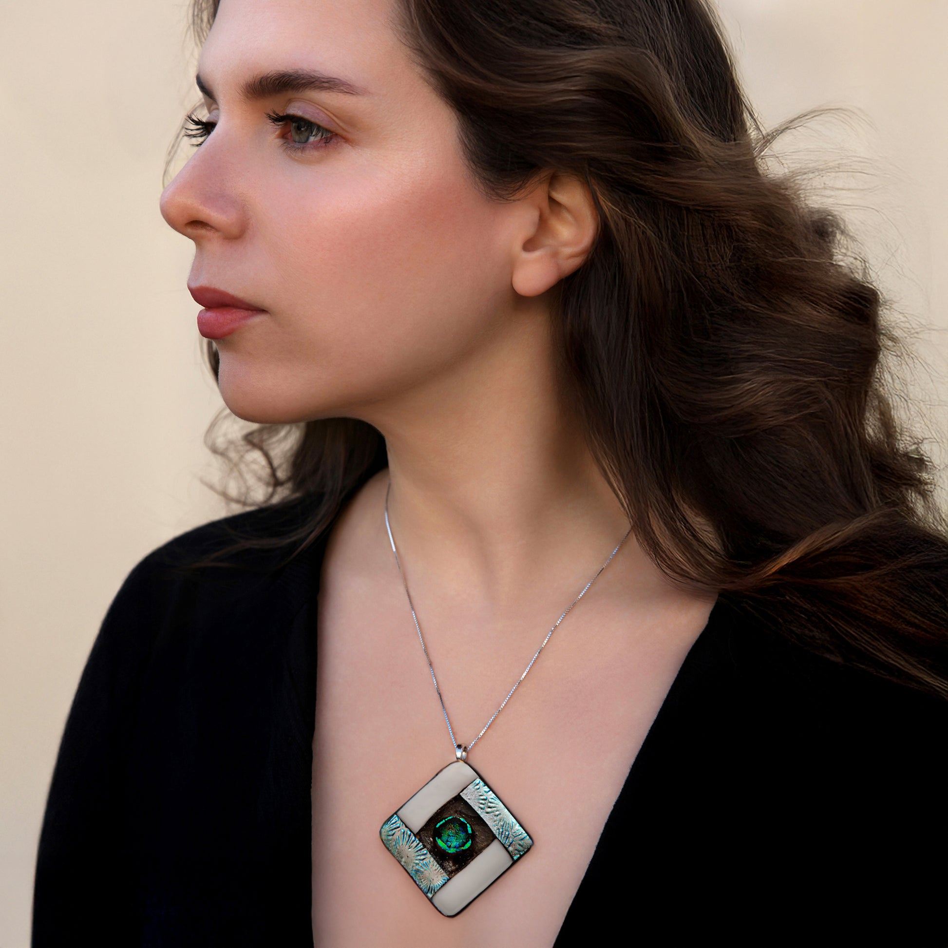 Model wearing the Elementa Air necklace by Invoke London, featuring a handcrafted diamond-shaped fused dichroic glass pendant in shimmering whites and silvers to symbolise clarity, lightness, and peace.
