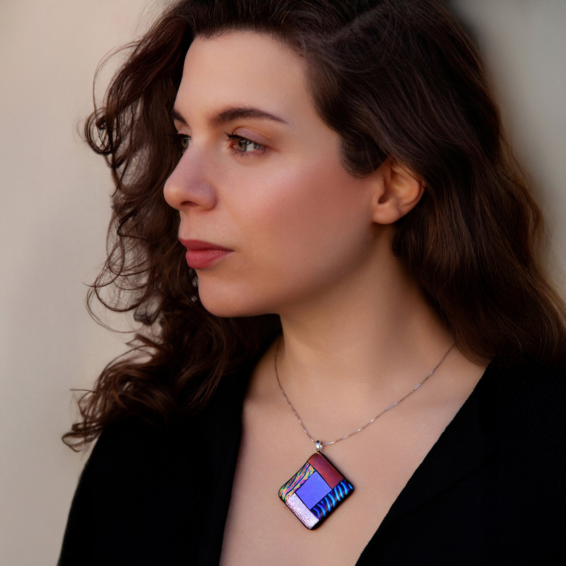 Model wearing the Elementa Combination necklace by Invoke London, a striking fused glass piece featuring Earth, Air, Fire, and Water colours in a diamond-shaped pendant, celebrating balance and nature's harmony.