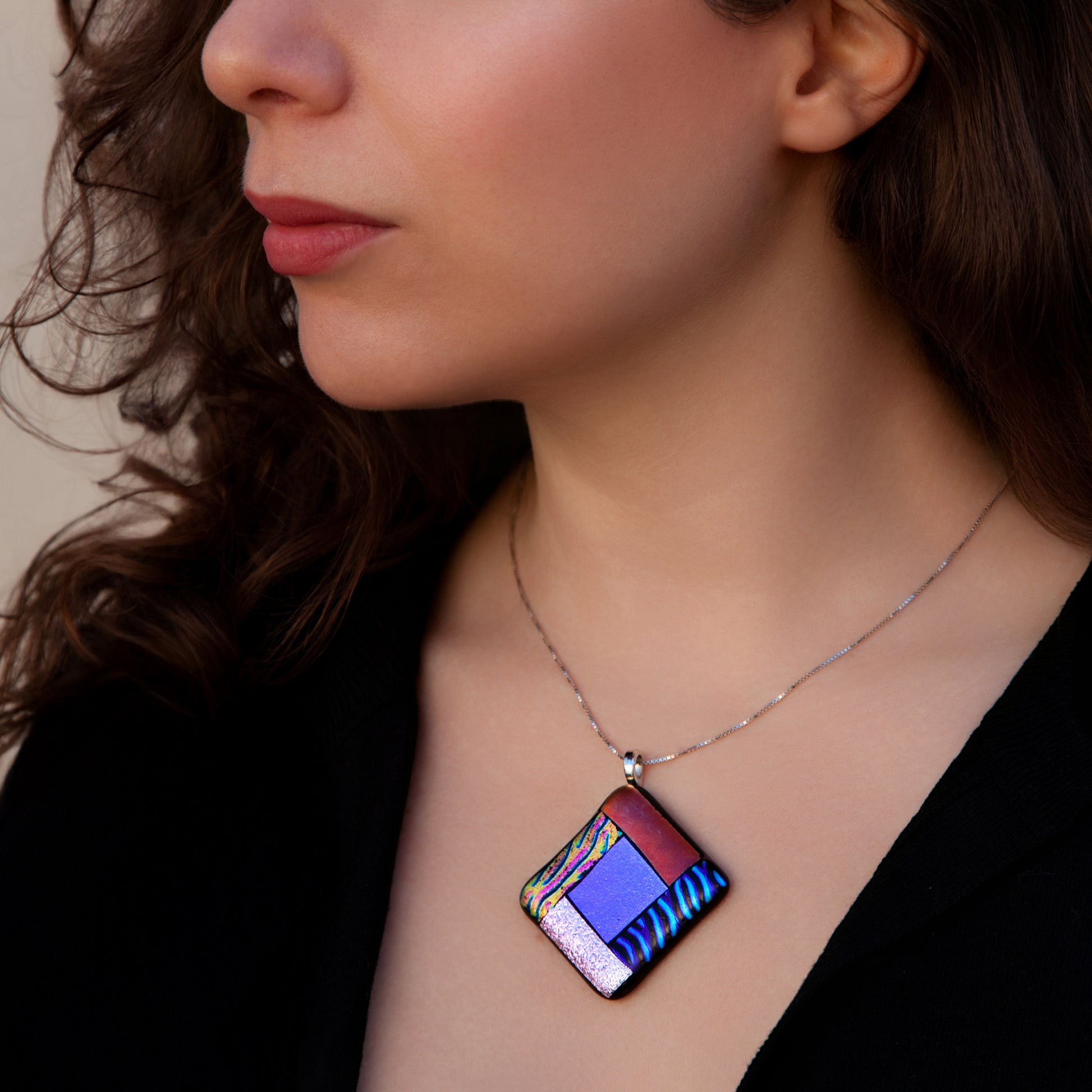 Close-up of model wearing the Elementa Combination necklace by Invoke London, showcasing a vibrant fused glass design in red, green, blue, and white to represent the four natural elements.