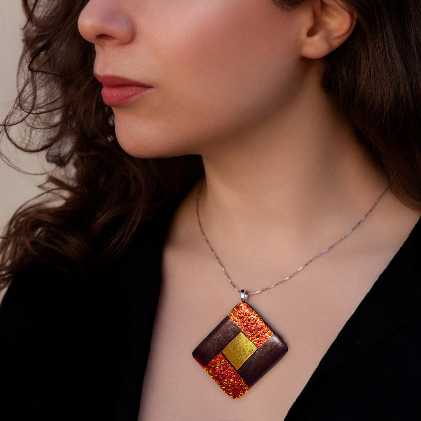 Close-up of model wearing Elementa Fire necklace by Invoke London with bold red-gold fused glass pendant symbolising energy and courage.