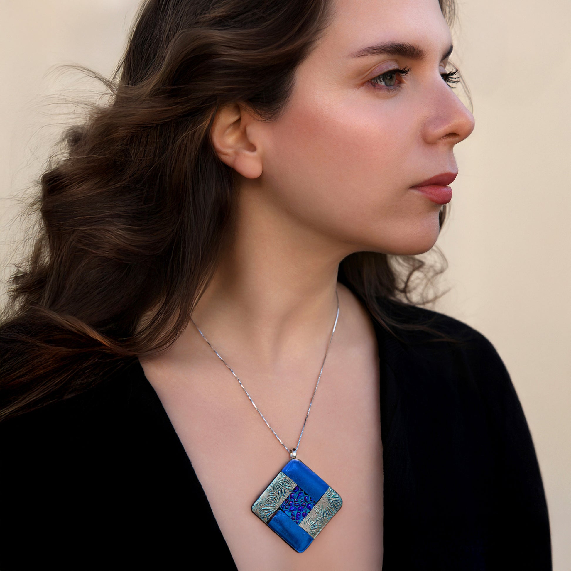 Model wearing Elementa Water necklace by Invoke London with deep blue fused glass pendant in silver, symbolising calm.