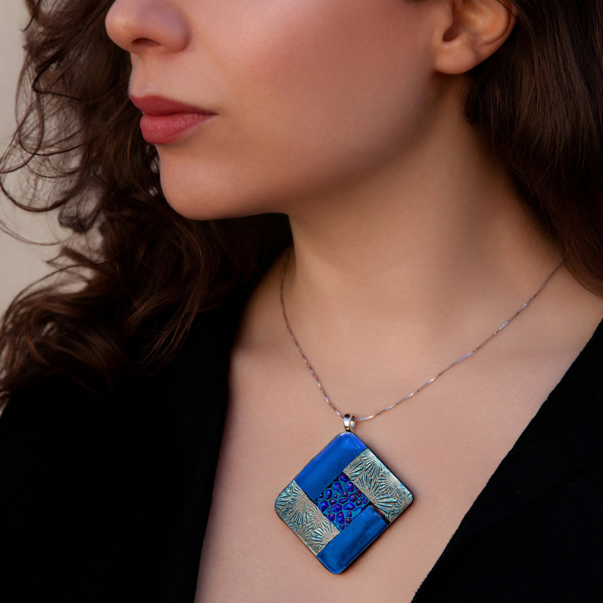 Close-up of model wearing Elementa Water necklace by Invoke London with deep blue fused glass pendant in silver, symbolising calm.