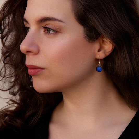 Close-up of a woman wearing a blue drop earring with a neutral background