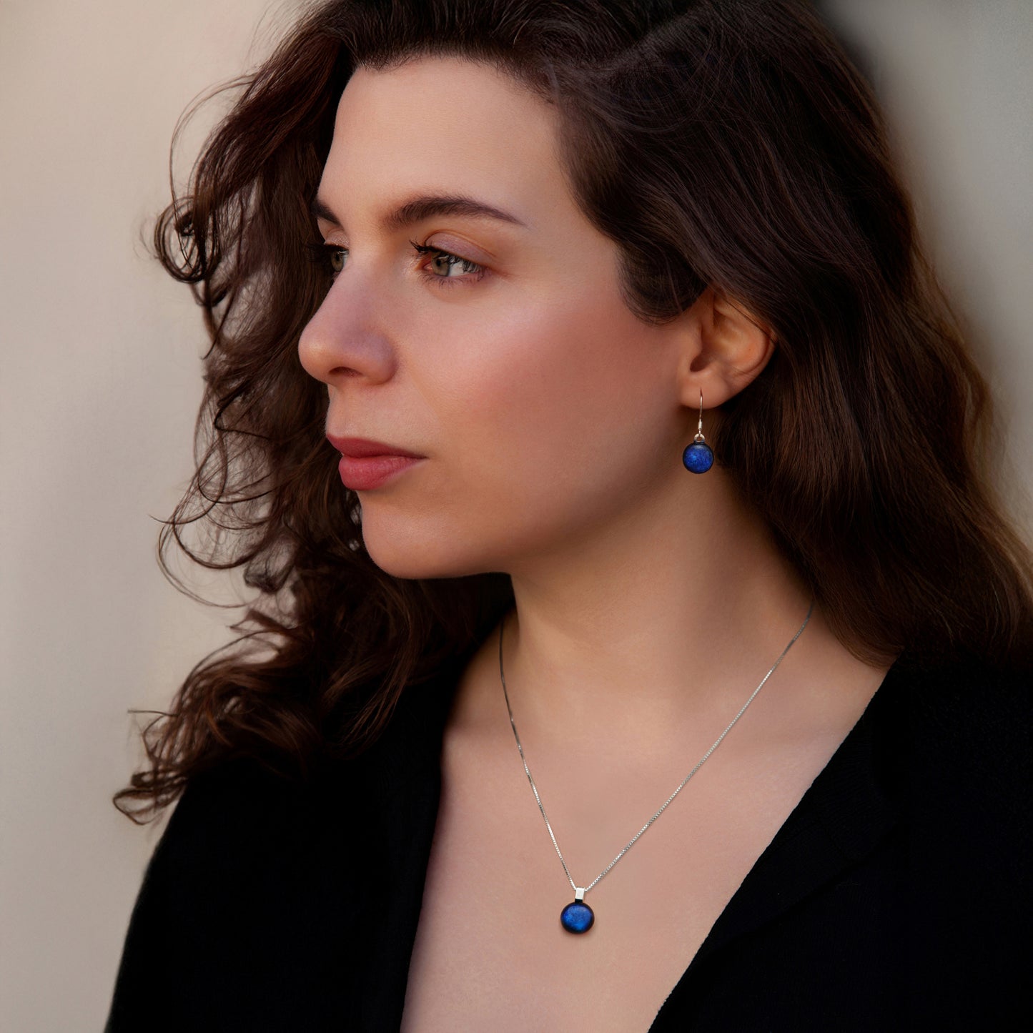 Woman wearing a matching drop earrings and necklace set against a neutral background