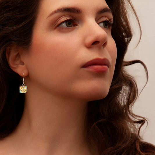 Close-up of a woman wearing a gold drop earring with a neutral background