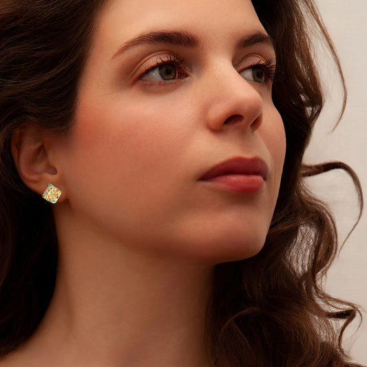 Close-up of a woman wearing a gold cube stud earring on a beige background