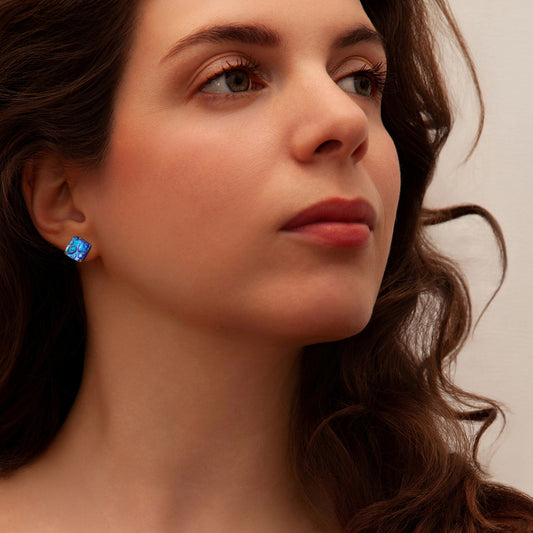 Close-up of a woman wearing blue cube stud earrings with a neutral background
