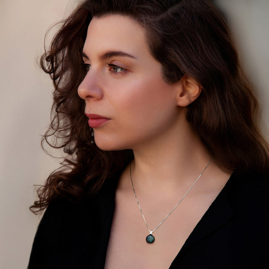 Woman wearing a necklace with a green pendant against a neutral background