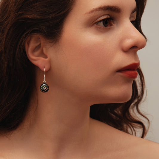 Close-up of woman wearing round black dichroic glass drop earrings with red square shimmer from the Orb collection by Invoke London.