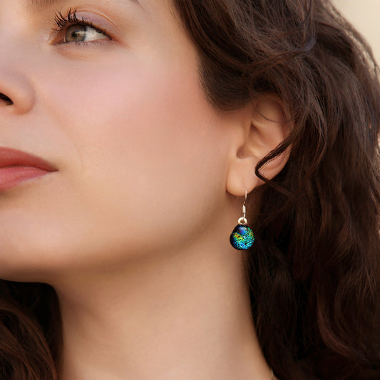 Close-up of model wearing green and gold ripple dichroic glass drop earrings.