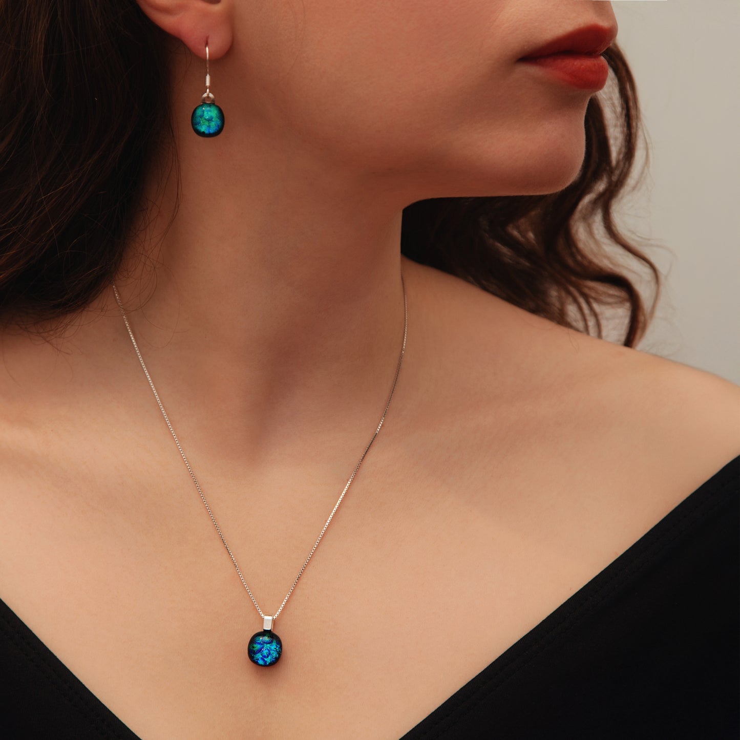Close-up of a woman wearing a silver necklace with blue pendant and matching earrings.