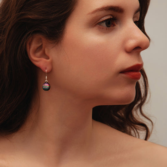 Close-up of woman wearing pink rainbow dichroic glass drop earrings from the Orb collection by Invoke London – handmade in London.