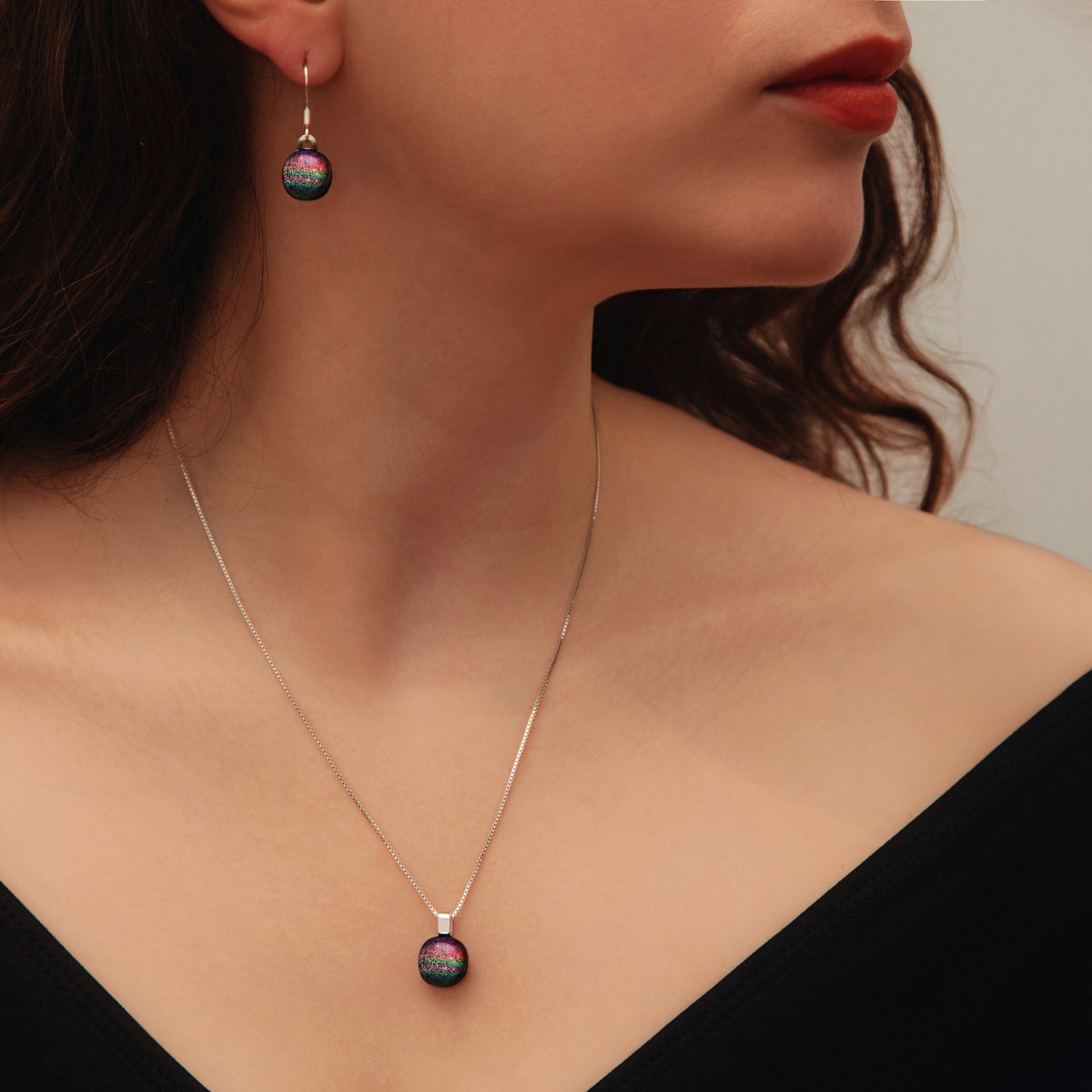 Woman wearing matching pink rainbow dichroic glass drop earrings and round pendant necklace from the Orb collection by Invoke London.
