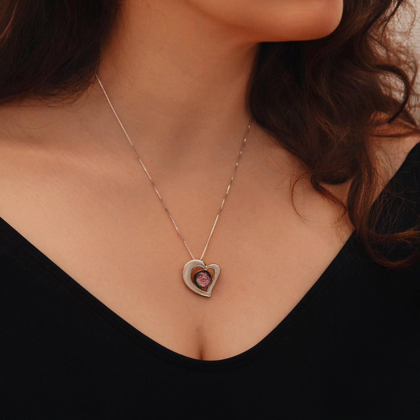 Close-up of luminous pink dichroic glass cabochon set in a heart-shaped silver-plated pendant, shimmering with colour-shift detail.