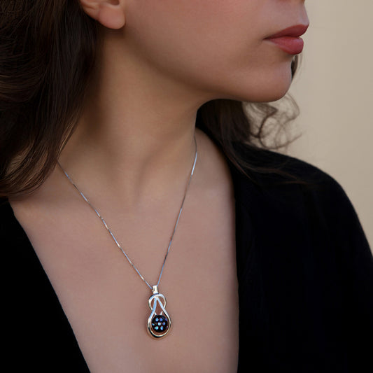 Close-up of a teardrop knot shaped Stella necklace with a black fused glass cabochon dotted with shimmering blue dichroic accents, handmade by Invoke London.