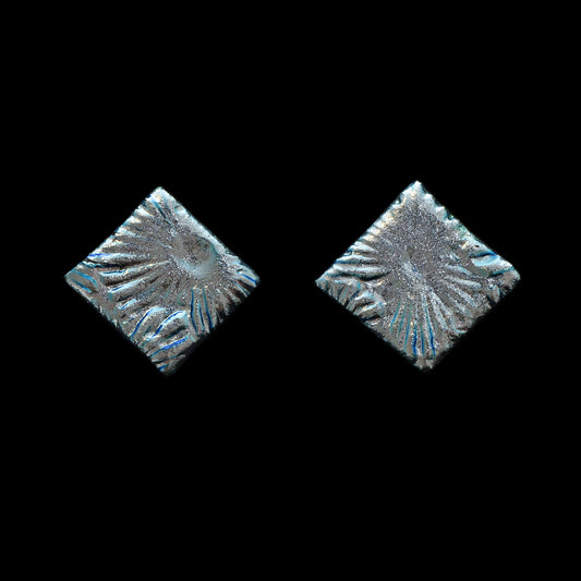 Square stud earrings made from shimmering silver dichroic glass with a sunburst texture, part of the Astra collection by Madiha Zaidi.