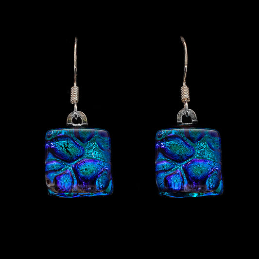 A pair of blue dew drop dichroic glass cube drop earrings with sterling silver hooks, against a black background.