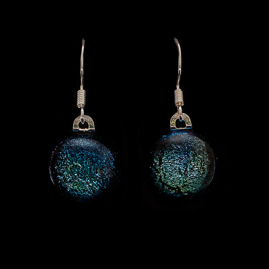 A pair of orb drop earrings with dichroic glass set in silver, displaying a blue and green color shift on a black background.