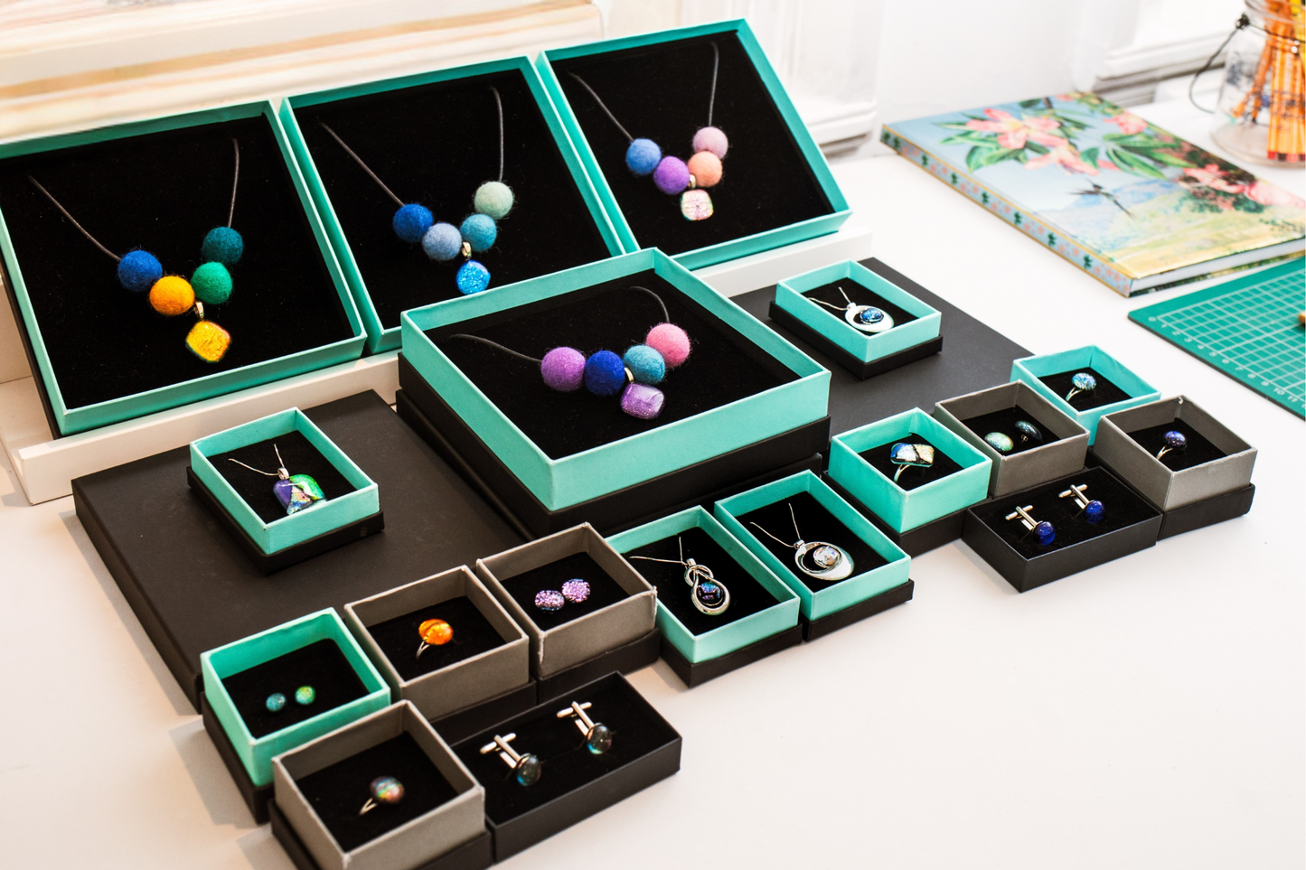 Handmade dichroic glass jewellery by Invoke London beautifully presented in eco-friendly gift boxes, including necklaces, rings, earrings and cufflinks, displayed on a white surface.