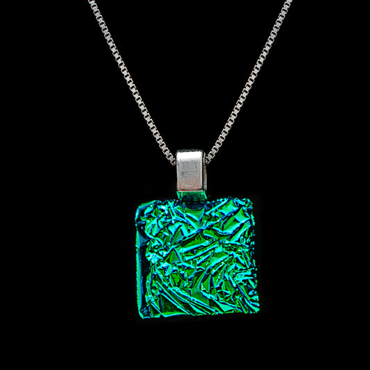 Square green crinkled dichroic glass pendant necklace on a silver chain. Handmade by Invoke London, this shimmering glass piece reflects vibrant emerald and teal tones from the Astra collection.