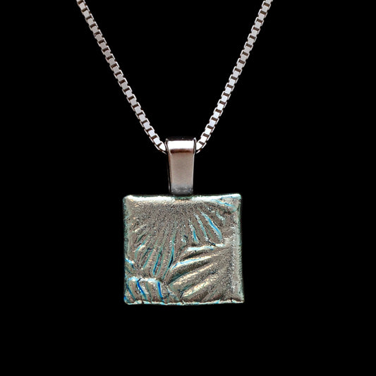 Handmade square pendant in silver dichroic glass with a radiating sunburst design, on a sterling silver chain from Invoke London's Astra collection.