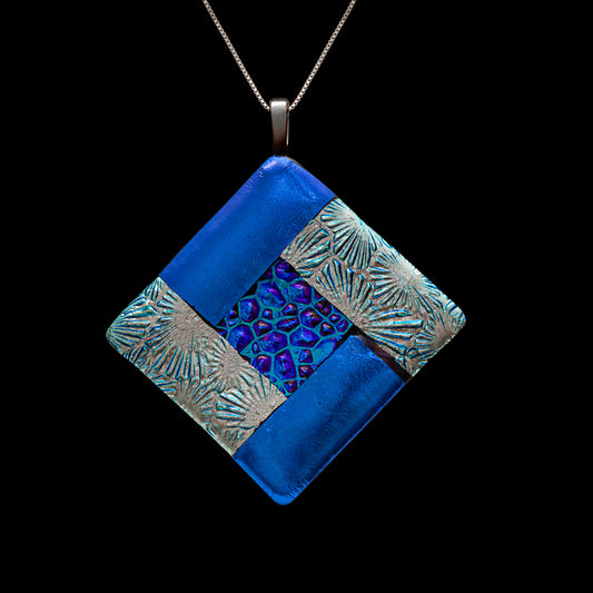 Close-up of a handmade diamond-shaped fused glass necklace in blue tones with silver textured bands and a central dichroic glass pattern symbolising the water element, from the Elementa Collection by Invoke London.