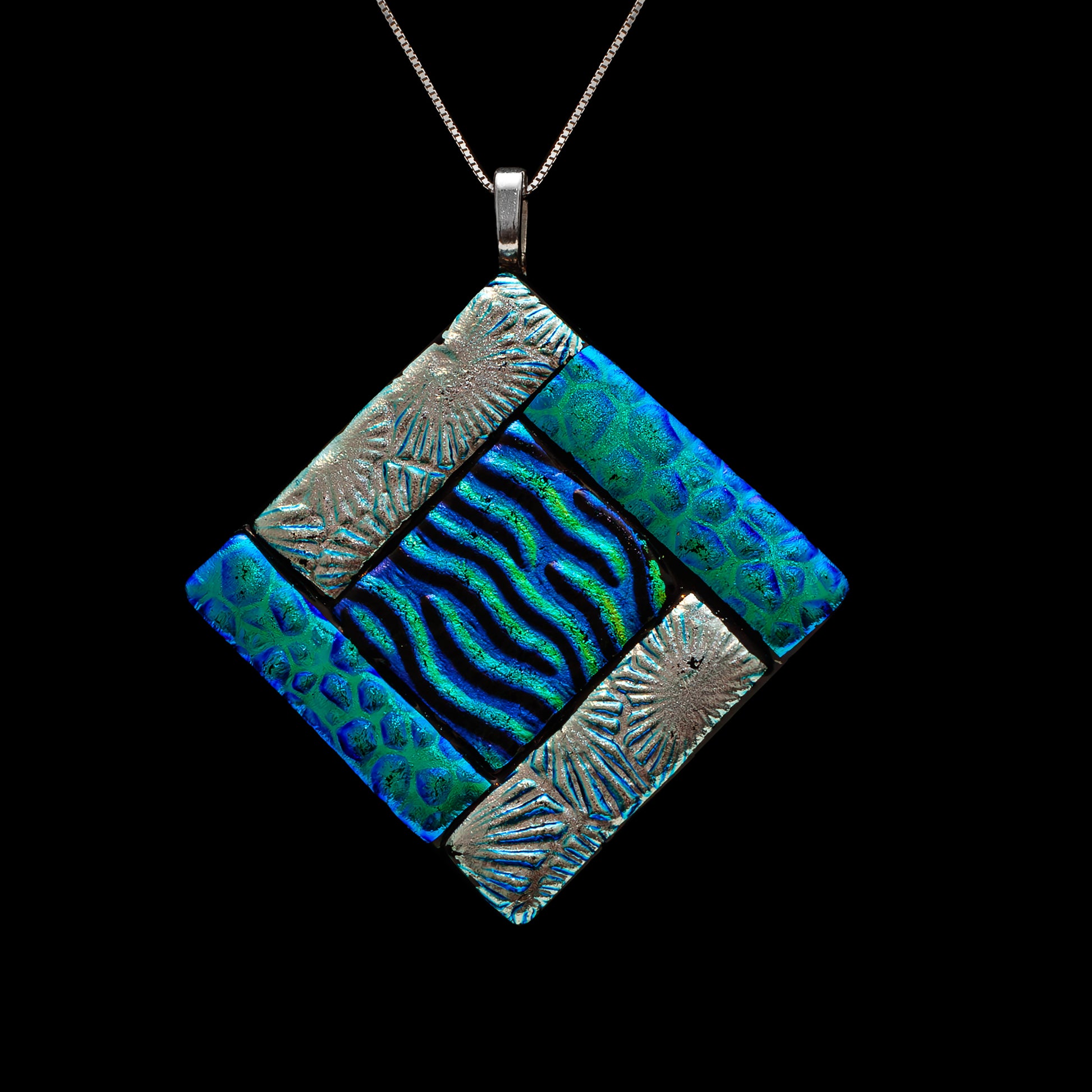 Close-up of a green fused glass diamond-shaped pendant with embossed silver segments and a central wavy dichroic glass design, inspired by the earth element, from the Elementa Collection by Invoke London.