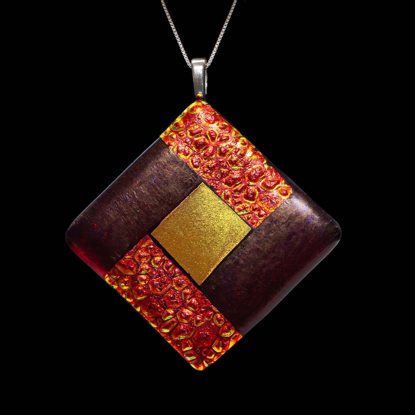 Close-up of a fused glass diamond pendant in deep red and gold tones with a glowing textured centre symbolising fire, from the Elementa Collection by Invoke London.