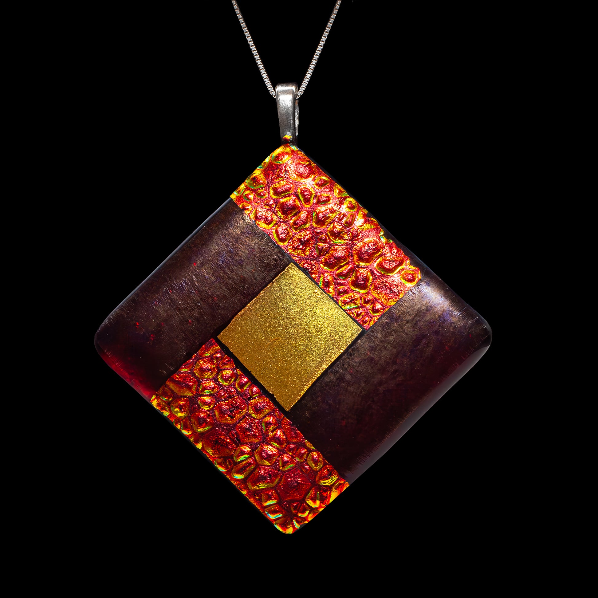 Close-up of a fused glass diamond pendant in deep red and gold tones with a glowing textured centre symbolising fire, from the Elementa Collection by Invoke London.