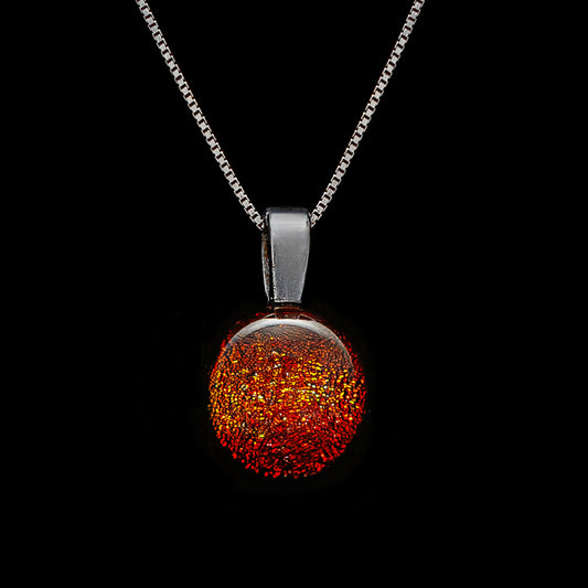 A round orange dichroic glass pendant necklace with a silver chain, displayed against a black background.