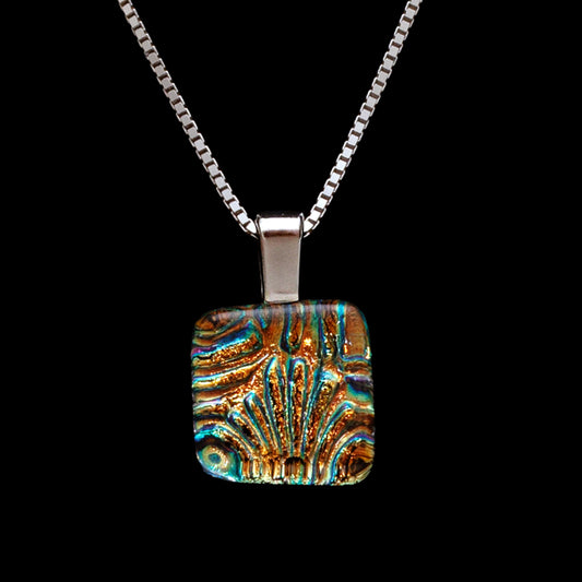 A handcrafted glass pendant necklace with a geometric pattern in gold and green hues on a black background, suspended from a silver chain.